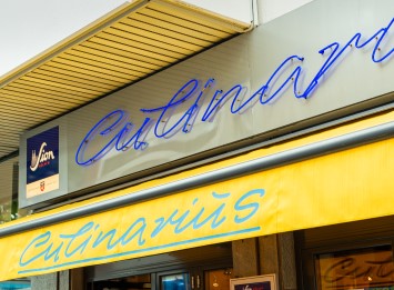 Eine Ladenfront mit leuchtender Schrift unter einem gelben Vordach.