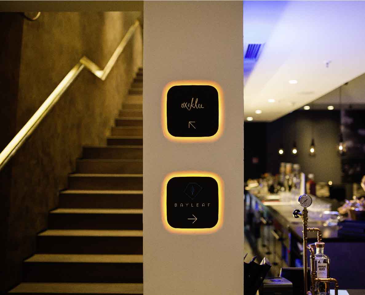 Eine beleuchtete Steintreppe führt nach links, daneben ein Pfeiler mit beleuchteten Wegweisern.