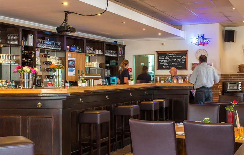 Eine Bar mit dunklen Holzmöbeln, Gästen und Bedienung, Getränke auf der Theke.