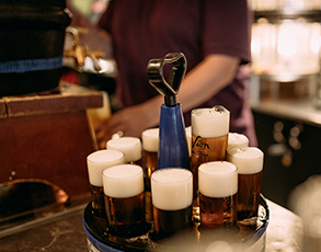 Eine Person serviert ein Tablett voller Biergläser in einer Bar.