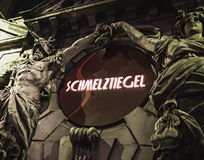 Statuen an einem Gebäude halten ein Schild mit der Aufschrift Schmelztiegel.