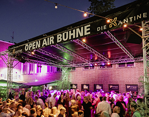 Eine Menschenmenge steht vor einer beleuchteten Freiluftbühne bei Nacht.