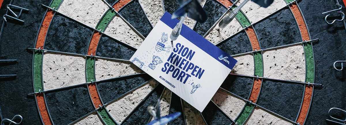 Eine Dartscheibe mit einem Flyer in der Mitte ist an einer Wand befestigt.