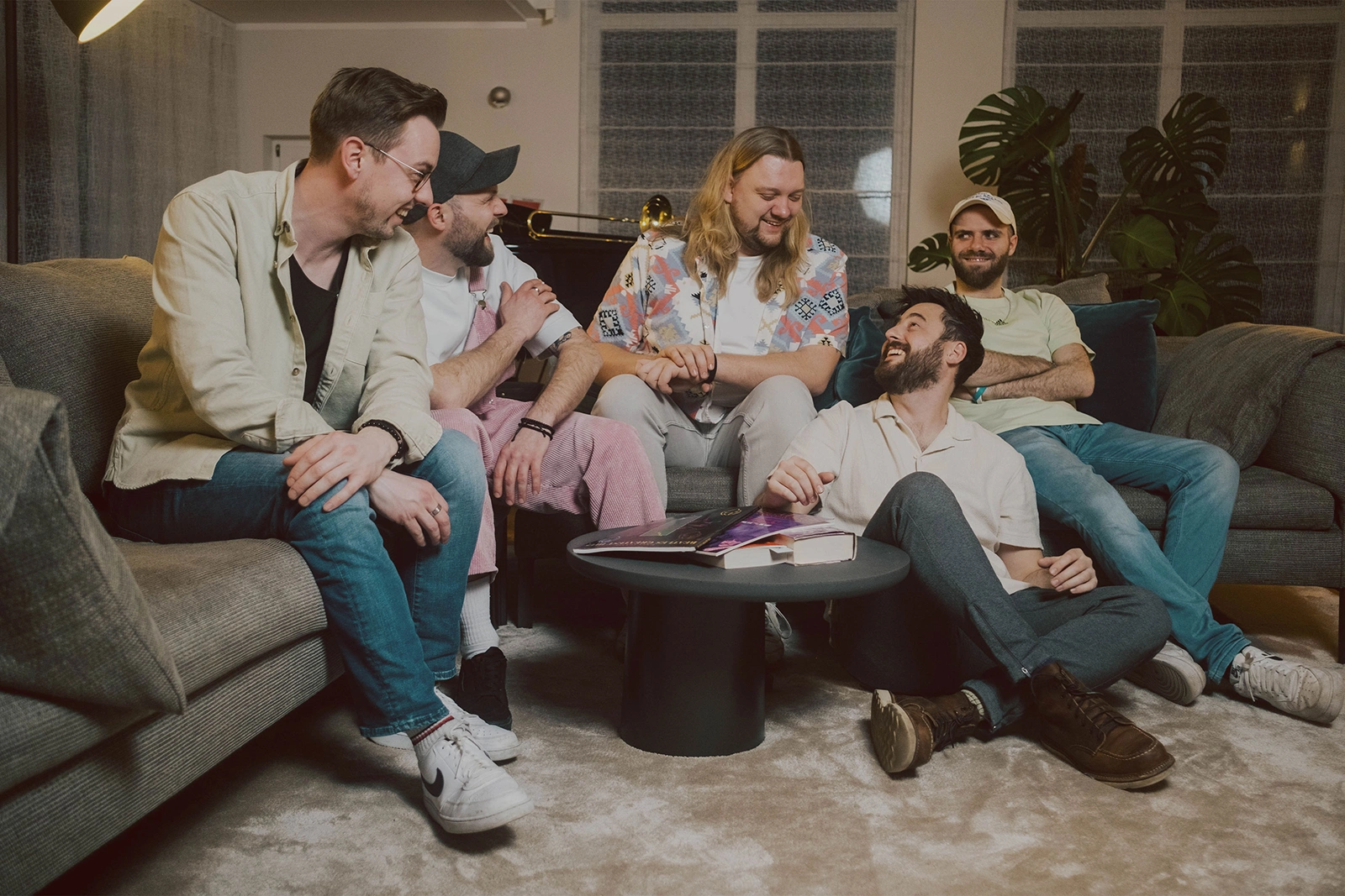 Eine Gruppe von fünf Männern sitzt auf einem Sofa und unterhält sich fröhlich in einem gemütlichen Wohnzimmer.