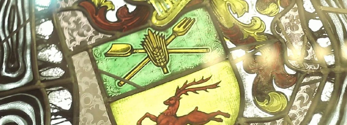 Ein Buntglasfenster zeigt ein Wappen mit Hirsch und Ähren auf grünem Hintergrund.