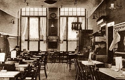 Ein historisches Restaurantinterieur mit holzgetäfelten Wänden und mehreren besetzten Tischen.