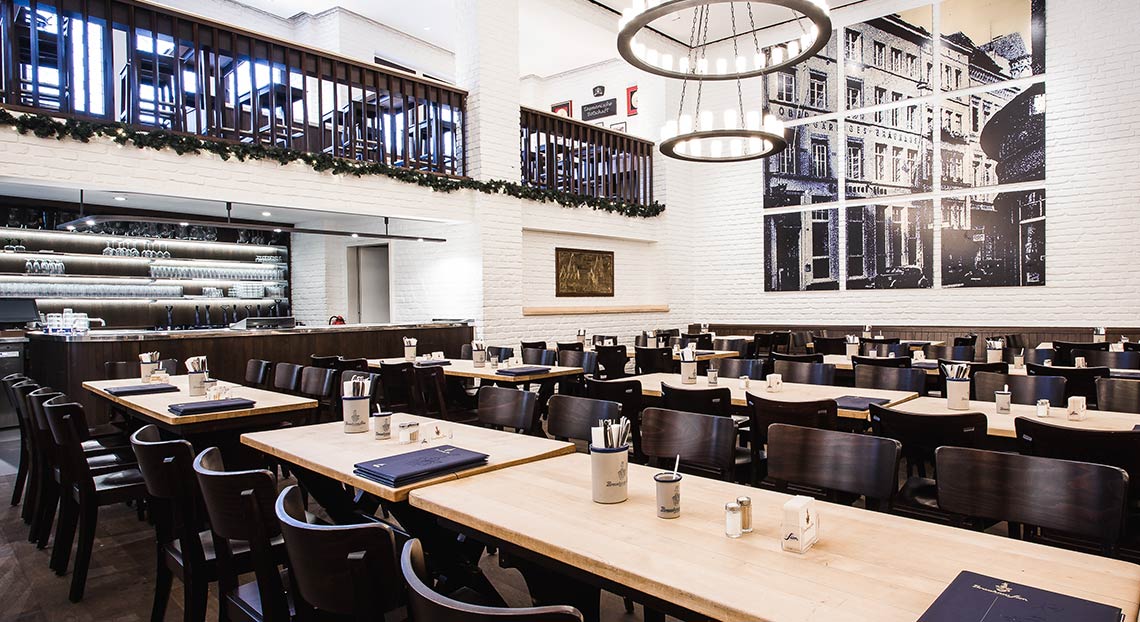 Ein großes, helles Restaurant mit Holztischen und dunklen Stühlen. An den Wänden hängen großformatige Bilder.