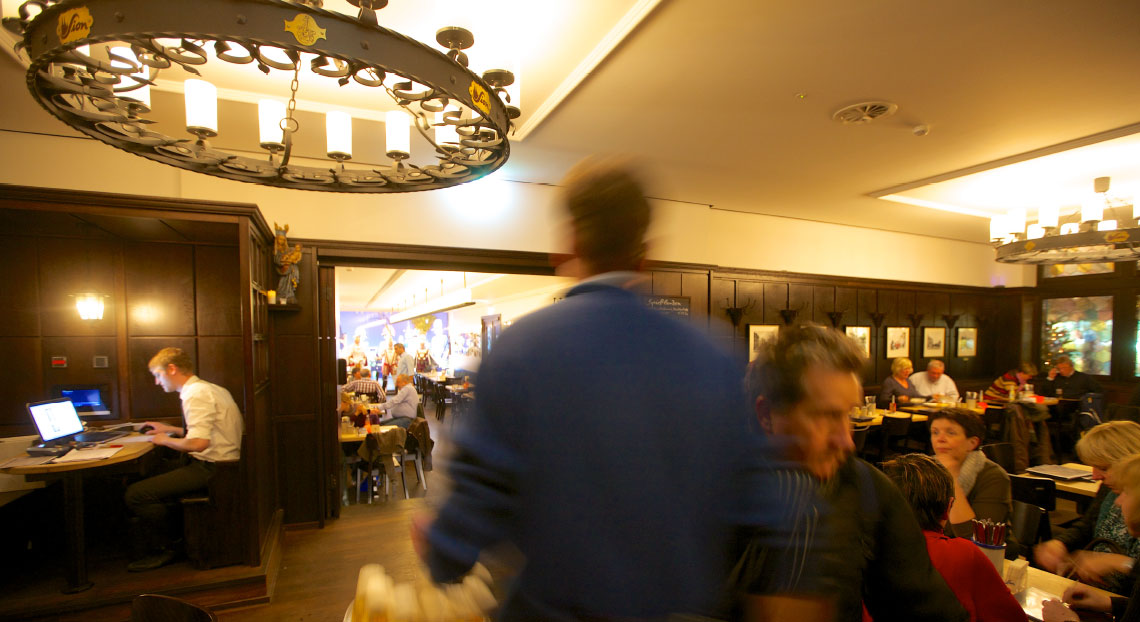 Ein belebtes Restaurant mit Gästen beim Essen, ein Mann arbeitet am Laptop.