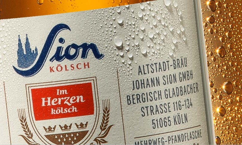 Nahaufnahme eines Bieretiketts mit Wassertropfen, Text im Vintage-Stil und goldener Hintergrund.